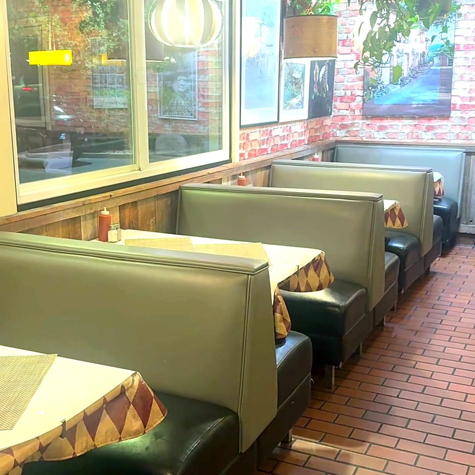 Row of green and black booths with set tables and hanging plants along the windows.