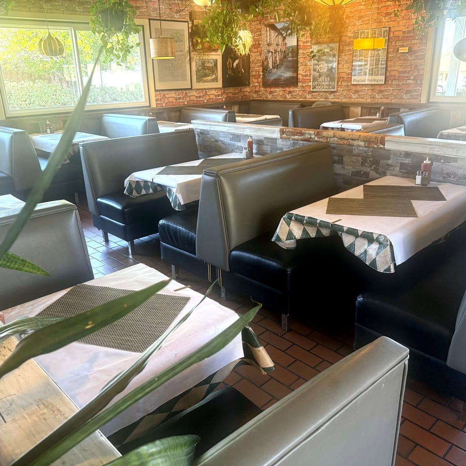 Dining room with booths, set tables, brick walls, and warm light.