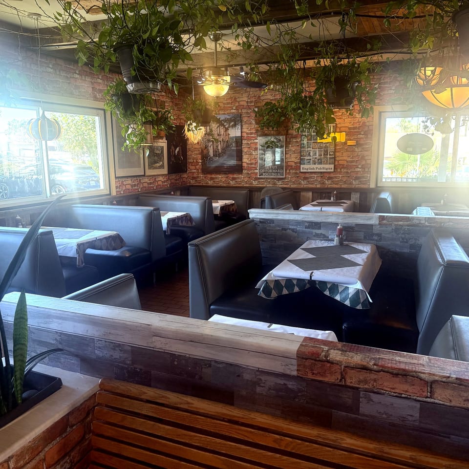 Restaurant interior with black booths, brick walls, hanging plants, and set tables.