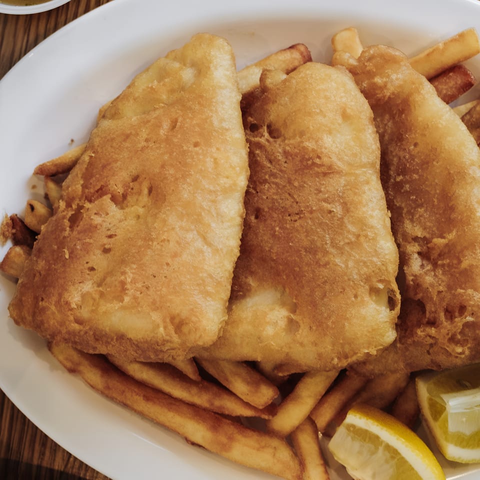 Three pieces of golden-brown fried fish and french fries with tartar sauce and lemon wedges.